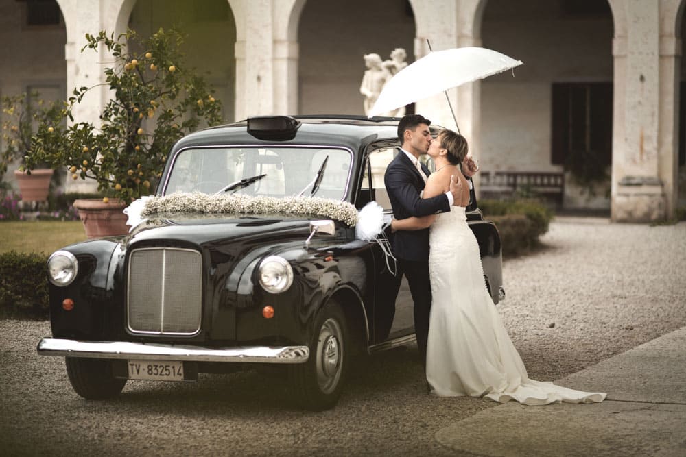 Immagine di sposi in cortile Ca marcello con ombrello e macchina storica, tempo piovoso